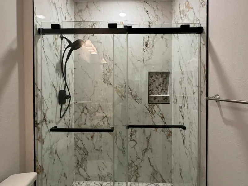 Walk-in shower with marble-look wall tile, white hex mosaic floor, black sliding glass door, and a recessed hex niche.