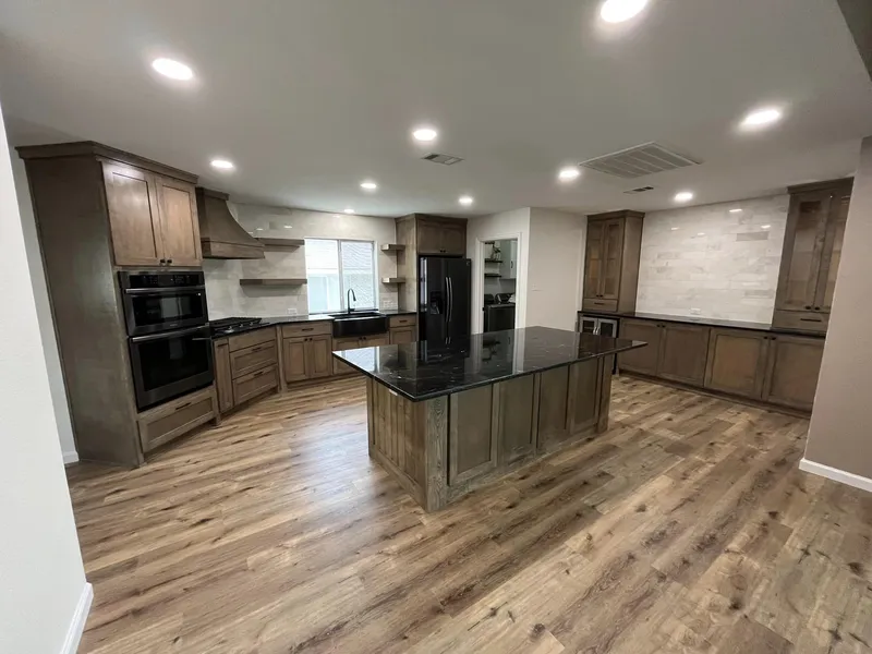 Open kitchen with wood-look plank flooring, stained cabinets, and a dark stone island.