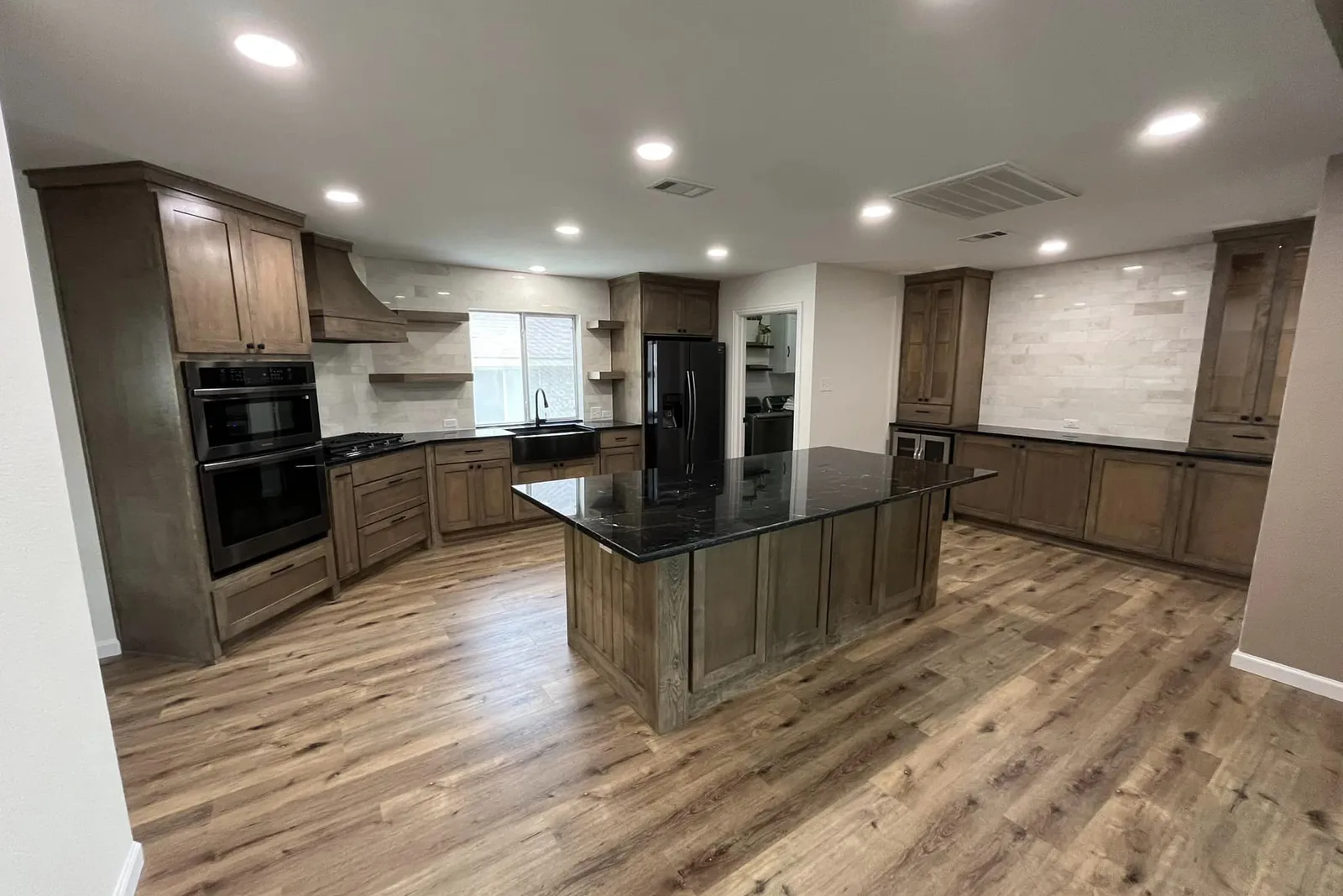 Finished kitchen with stained wood cabinets, a black stone island, and hardwood floors.