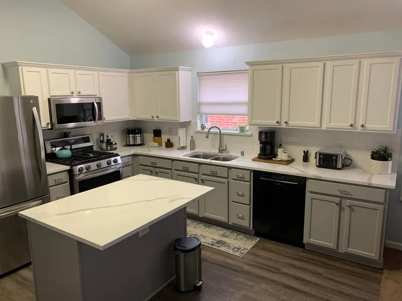 U-shaped kitchen with white uppers, gray-painted bases, white counters and island, and a subway backsplash.
