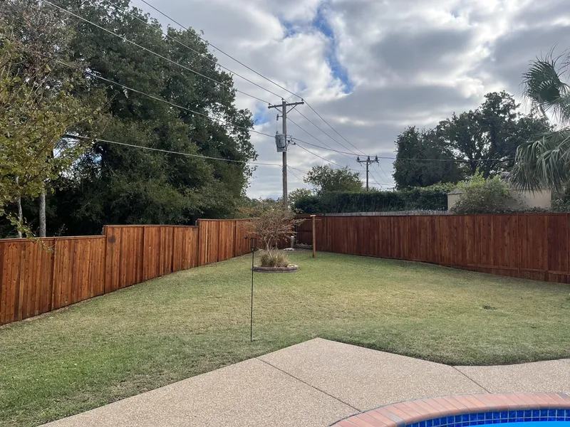 Stained cedar privacy fence around a grass yard, pool coping in the foreground.